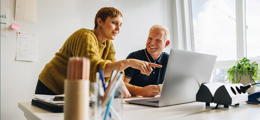 Woman helping man at desk on laptop